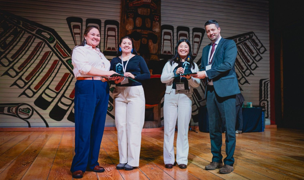 Four people stand on stage. Two of them are handing trophies to the other two.