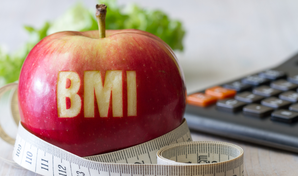 A red apple with the letters BMI carved into it and a measuring tape and calculator.