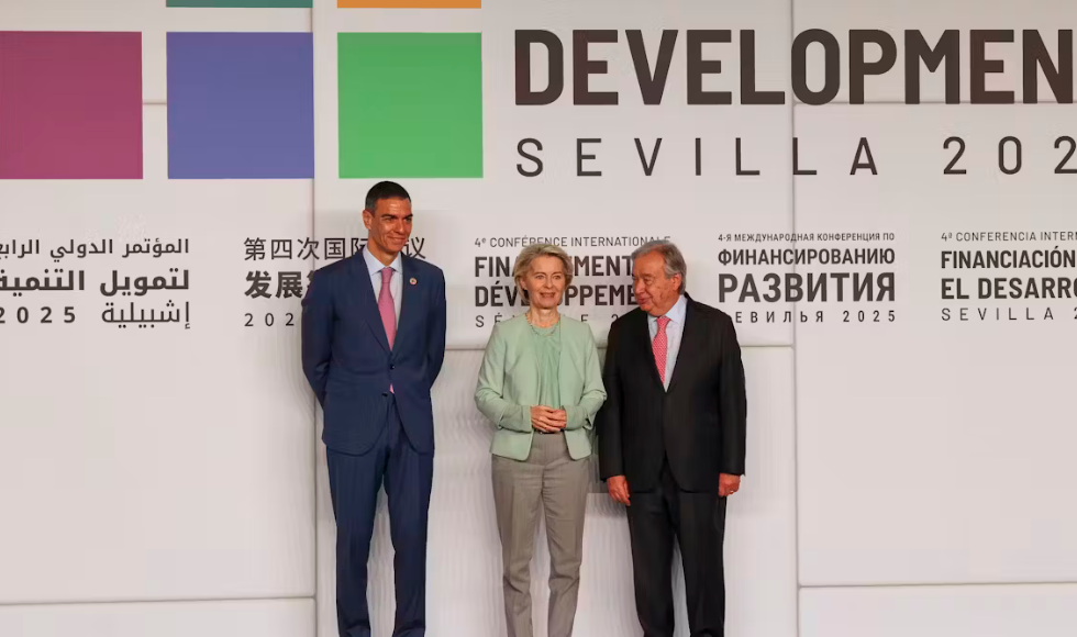 Three people stand in front of a wall that has writing in various languages on it.