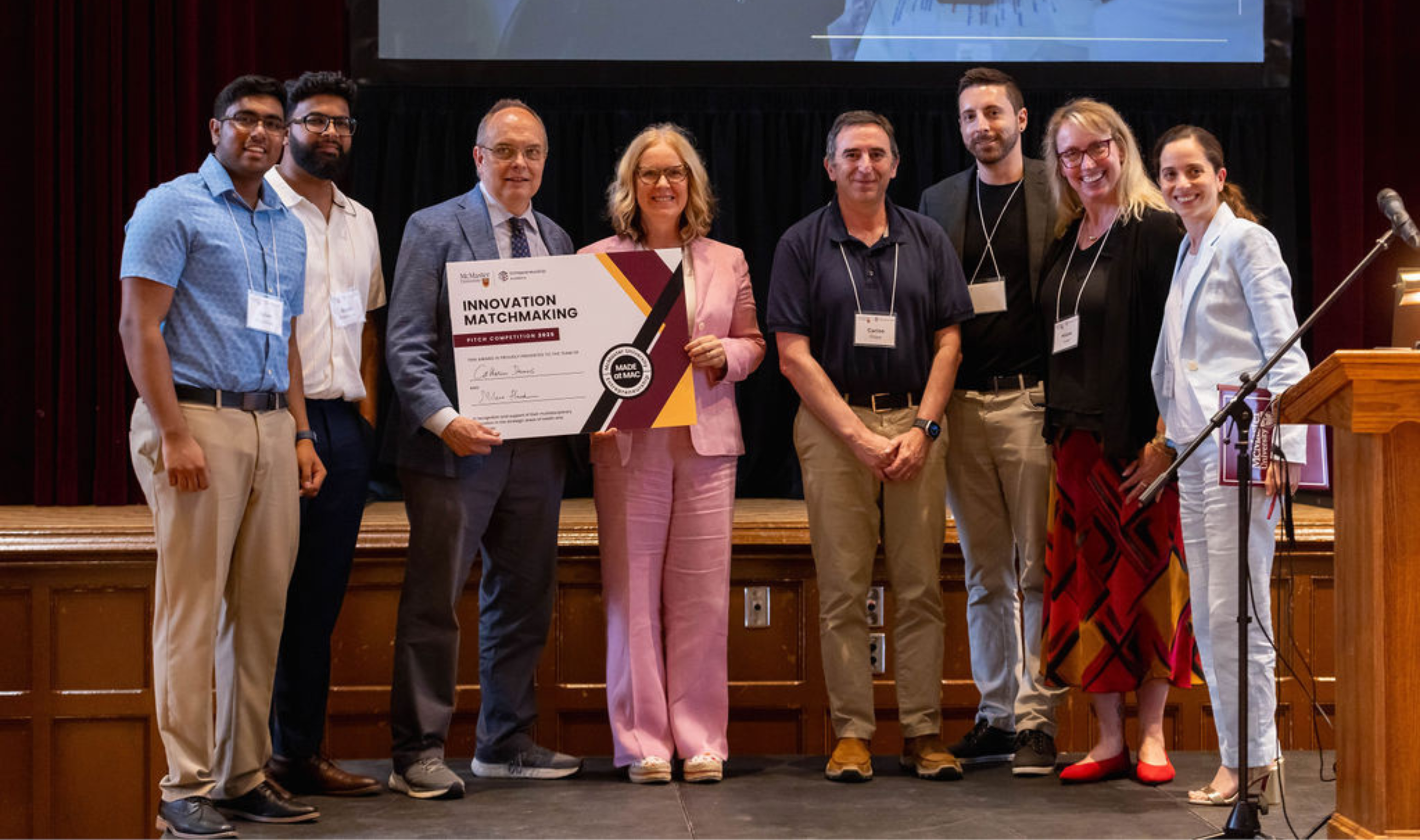 Eight people stand on stage, smiling and holding up an award plaque.