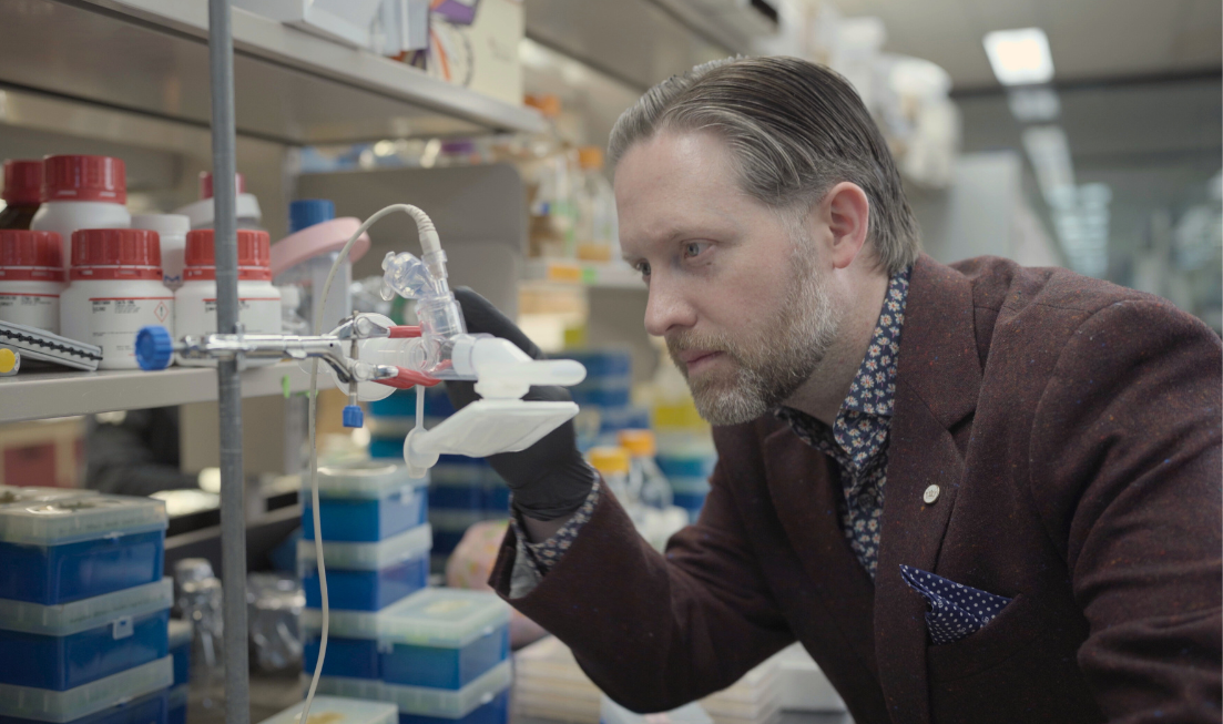 Matthew Miller leans down and looks at tubes and scientific apparatus in a lab setting.