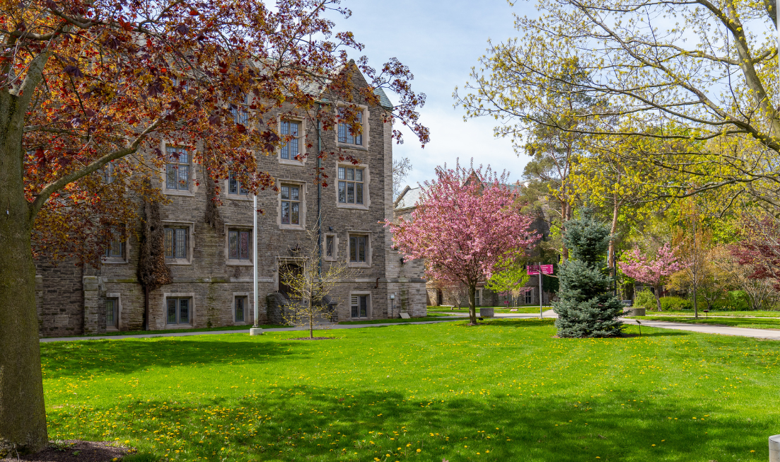 Exterior of a McMaster building in the spring, with green lawns and blossoming trees.