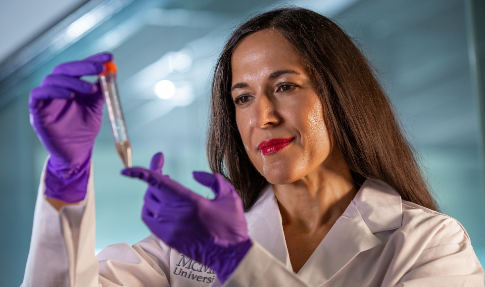A woman in a lab coat holds up a glass vial.