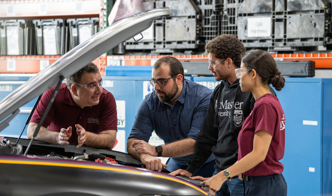 Professor Ali Emadi and three graduate students lean over a car with its hood open, chatting