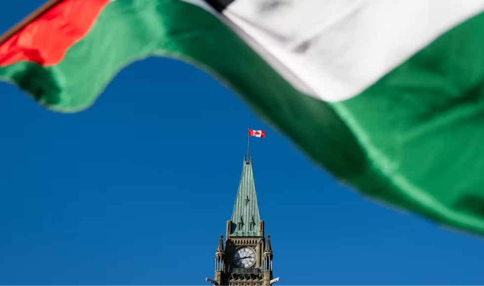 A Palestine flag, out of focus, is at the top of the frame. In the distance is the tower of an old building, with a Canadian flag flying on top.