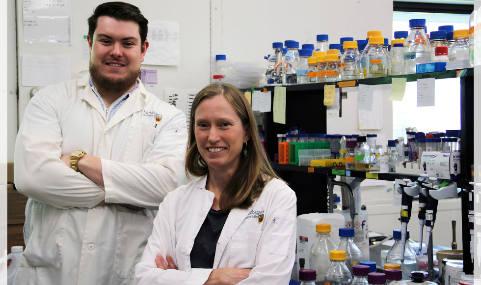 Two people in lab coats stand in a science lab, smiling.