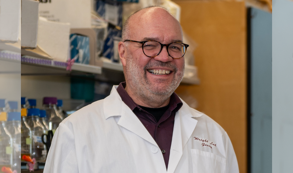 A man in a white lab coat and glasses smiles.