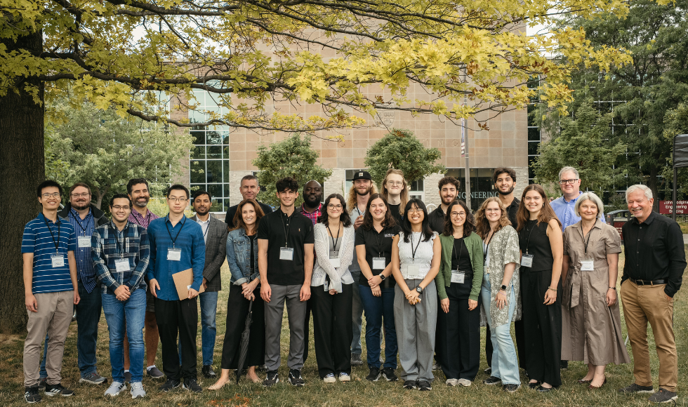 A group shot of many people, wearing dress clothes and name tags, standing on the lawn in front of a large building.