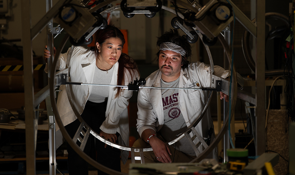 Two people in lab coats look at a metal hoop in a lab.